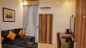 A modern living room with a sofa, a coffee table, a TV, and a wooden door. - Kashvalley Hotel and Suites (Lagos)