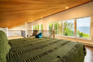 Un dormitorio con una cama grande, un balcón con una silla y vistas a árboles y montañas.