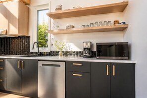 Moderni keittiö, jossa on mustat kaapit, astianpesukone, kahvinkeitin ja mikroaaltouuni.