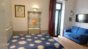 A bedroom with a bed, a blue sofa, a television, and a painting on the wall. - SALENTO SEA AND ART (Nardò)