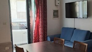 A living room with a sofa, a TV mounted on the wall, a dining table with chairs, and a window with curtains. - SALENTO SEA AND ART (Nardò)