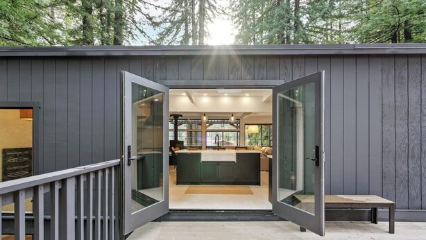 A modern cabin with a glass door entrance, a kitchen with a central island, and a view of the surrounding forest. - Relaxing Home Among The Redwoods - Dog-Friendly (Monte Rio)