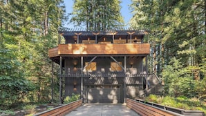 A two-story wooden cabin with a covered porch, surrounded by dense forest. - Relaxing Home Among The Redwoods - Dog-Friendly (Monte Rio)