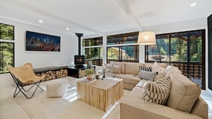 A modern living room with a large sofa, a coffee table, a fireplace, and large windows. - Relaxing Home Among The Redwoods - Dog-Friendly (Monte Rio)