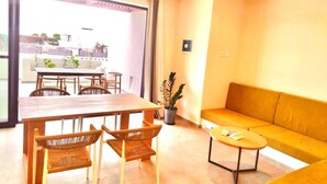 A modern living room with a wooden dining table, wicker chairs, a yellow sofa, and a potted plant.