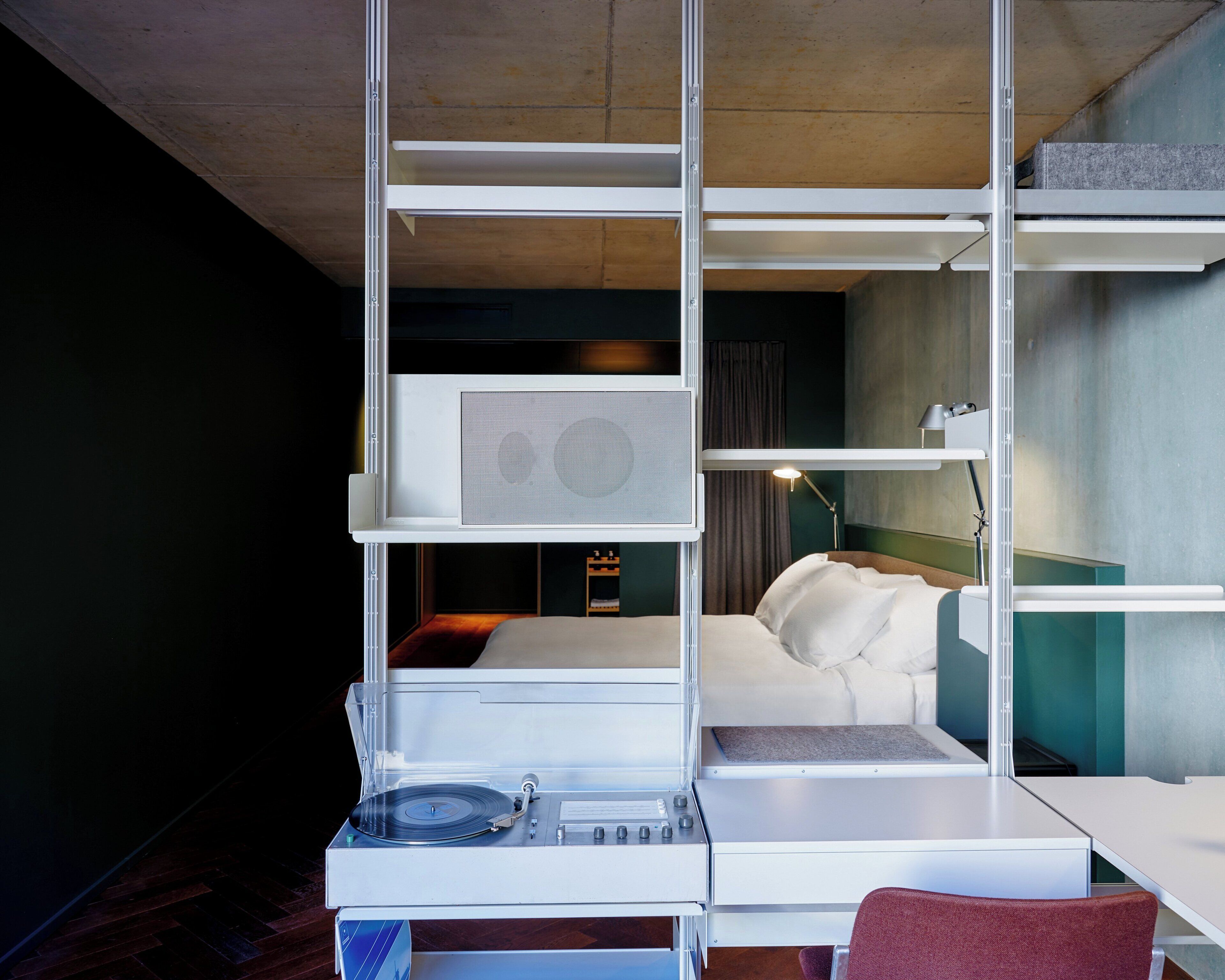 Ein modernes Hotelzimmer mit einem Bett, einem Schreibtisch mit Plattenspieler und einem großen Fenster.