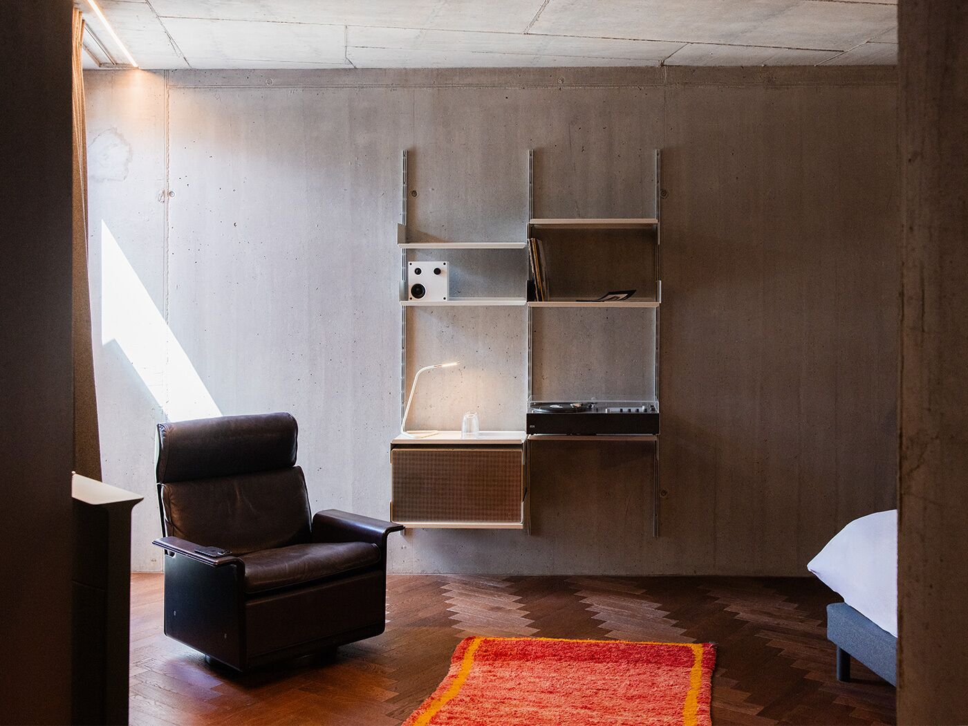 A modern room with a built-in desk, a leather chair, a bed, and a red rug.