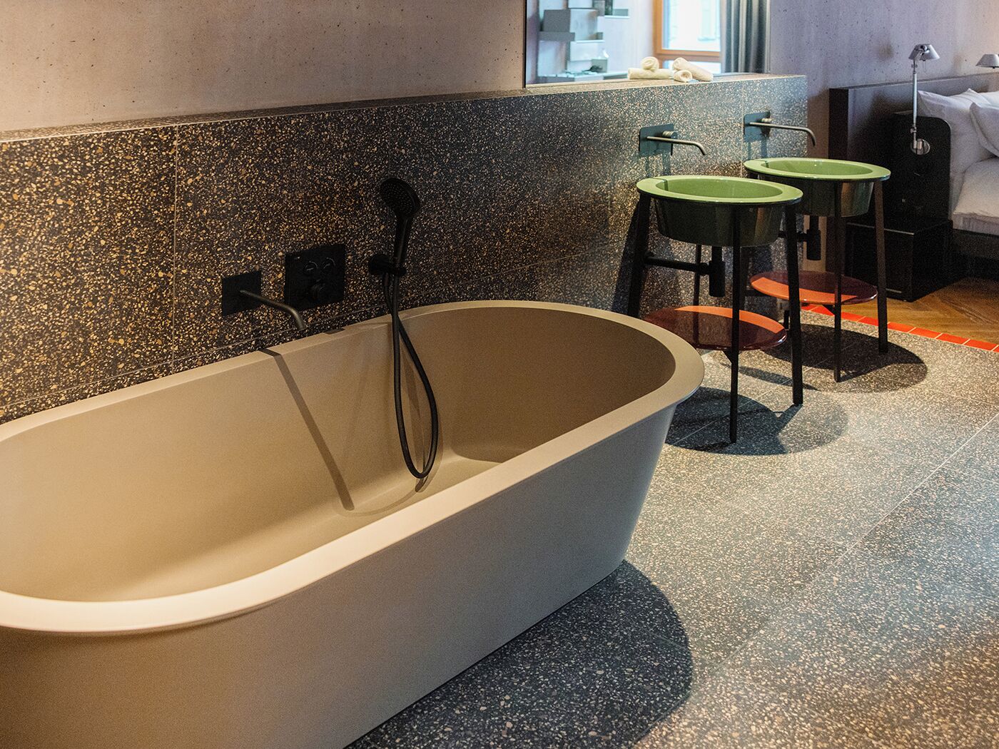 A modern bathroom with a freestanding bathtub, two green bar stools, and a large mirror above the sink.