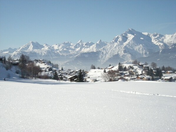 Un paisaje nevado con un pueblo y montañas cubiertas de nieve al fondo.