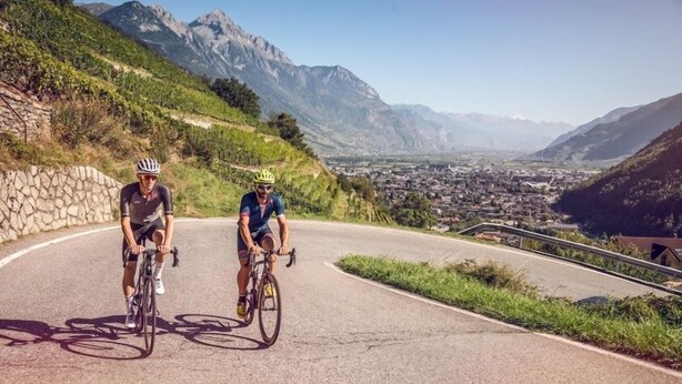 Two cyclists on a winding road with a mountainous backdrop. - Hôtel Borsari - A Member of Design Hotels (Martigny)