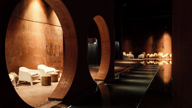 Un intérieur moderne avec des plafonds en arc de cercle, une allée centrale et des coins salon agrémentés de paniers en osier.