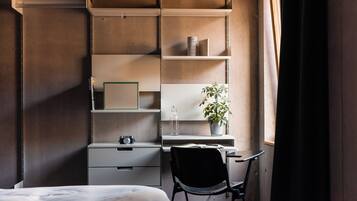 Un dormitorio con cama, escritorio con silla, estantería y planta en maceta.
