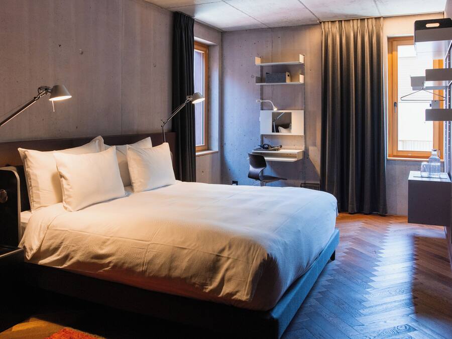 A modern hotel room with a large bed, bedside lamps, a desk, and a wardrobe.