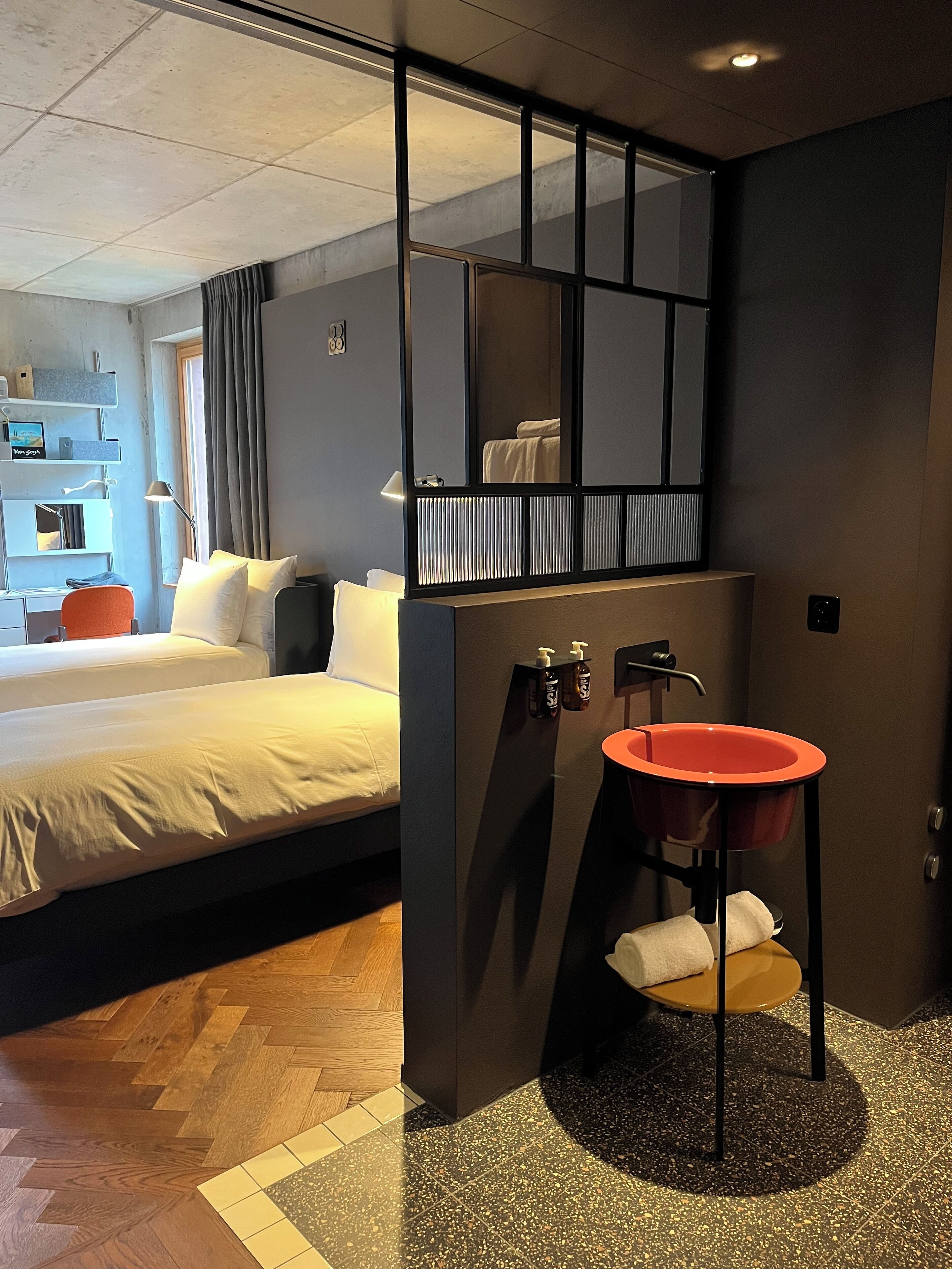 A hotel room with a bed, a desk, a mirror, a sink, and a shower area.