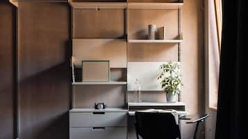 Een slaapkamer met een bed, een bureau met stoel, een plank met boeken en een plant, en een raam met gordijnen.