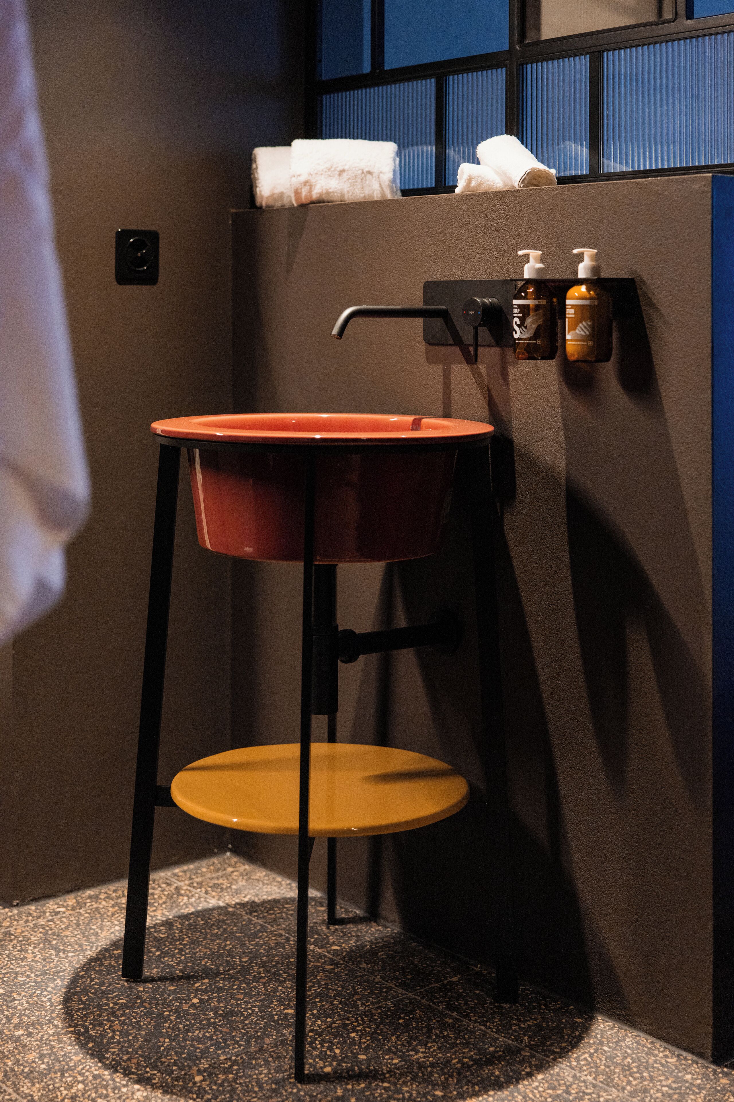 Un baño compacto con un taburete pequeño, un lavabo montado en la pared y un perchero para toallas.