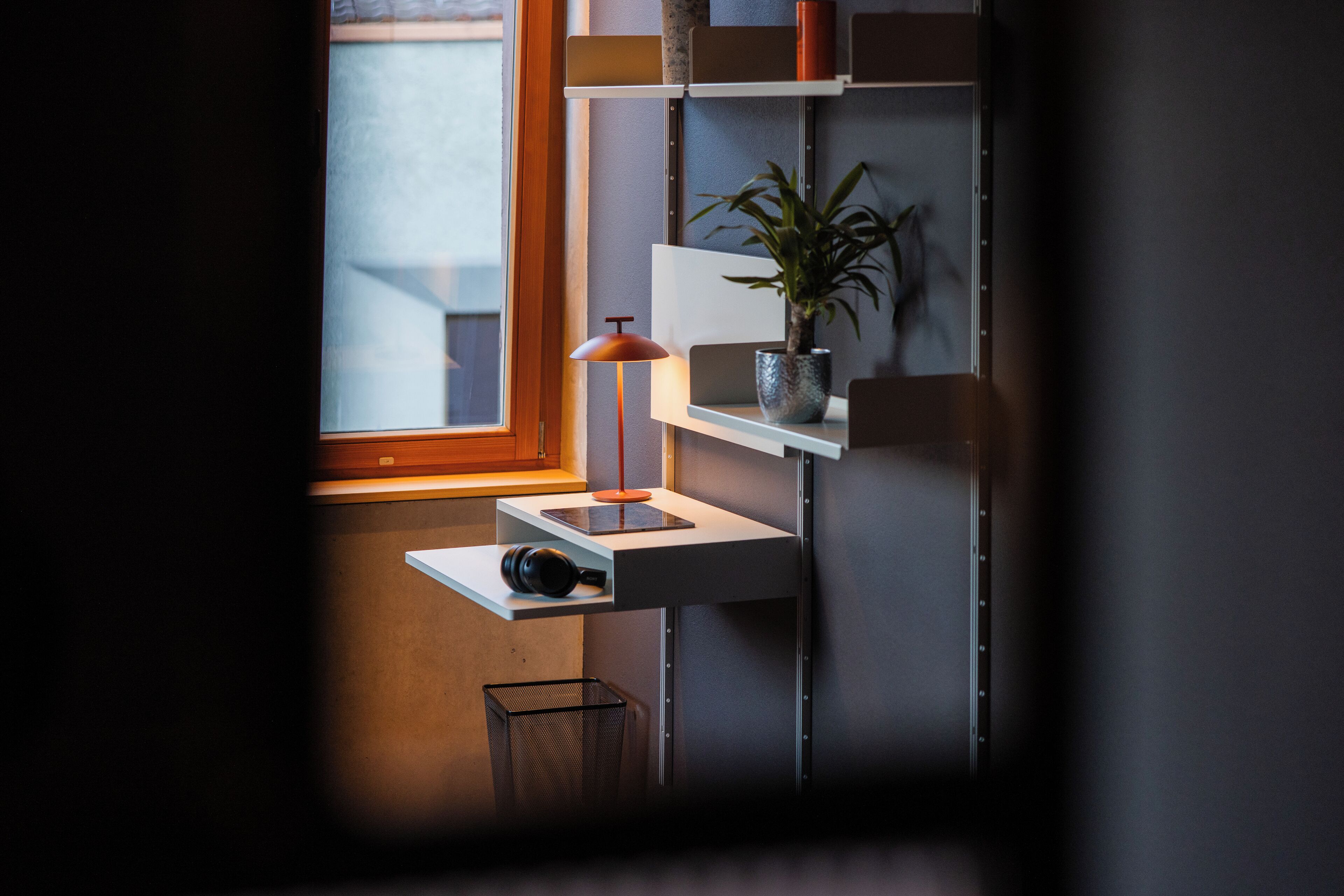 A modern workspace with a desk, a lamp, a potted plant, and a window.