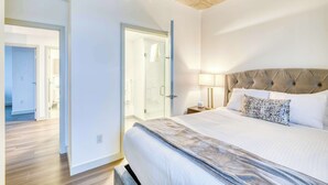 Ett hotellrum med en stor säng, ett stoppat sänggavell, en duschkabin med glasväggar och ett trägolv.