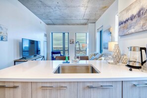 A modern kitchen with a large island, stainless steel sink, and a flat-screen TV. - Modern Apt In Kendall Square (Cambridge)