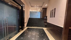 A modern hallway with a marble floor, a glass wall on the left, and a staircase at the end. - Hotel SB Castle  (Kanpur)