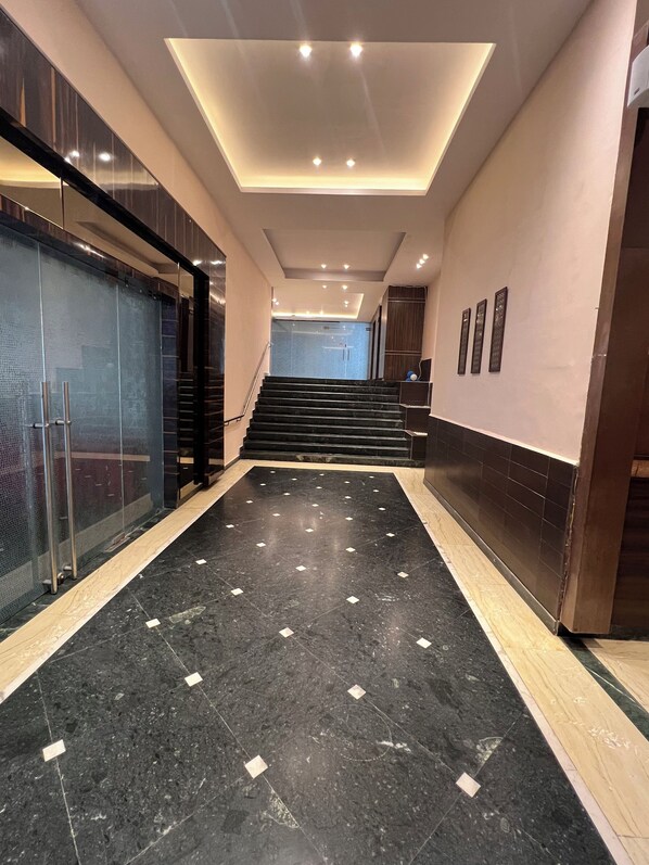 A modern hallway with a marble floor, a glass wall on the left, and a staircase at the end. - Hotel SB Castle  (Kanpur)
