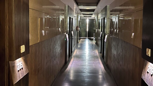 A corridor with dark wooden walls and a tiled floor, leading to a bright exit at the end. - Hotel SB Castle  (Kanpur)