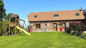 A house with a large front lawn, a wooden play structure, and potted plants.