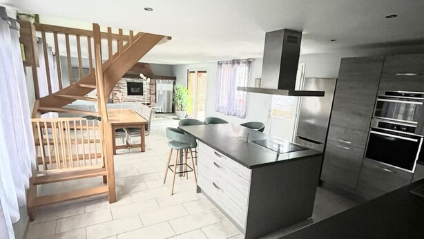 A modern kitchen with a central island, built-in appliances, and a wooden staircase.