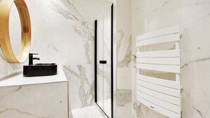 A bathroom with a marble wall, a black sink, a wooden-framed mirror, and a white towel rack. - An Atypical 1-BR in Place Vendôme Tuileries (Paris)