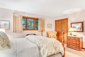 A bedroom with a bed, a wooden dresser, a chair, a window with curtains, and a mirror.