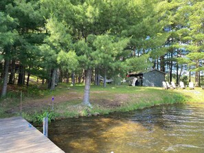 A cabin with a dock extending into a clear stream, surrounded by dense trees. - Loonsight - PET FRIENDLY (Minocqua)