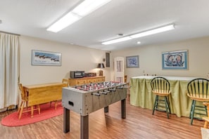 A room with a foosball table, a wooden table, and chairs. There are wall art pieces and a microwave on a cabinet. - Loonsight - PET FRIENDLY (Minocqua)