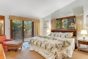 A bedroom with a large bed, a chair, a nightstand, and a view of a balcony.