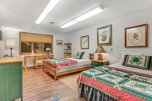 Une pièce avec un bureau en bois, deux lits avec des couvertures, une fenêtre et des œuvres d’art murales.