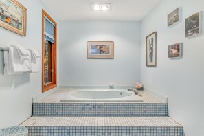 A bathroom with a large bathtub, tiled steps, and framed artwork on the walls.