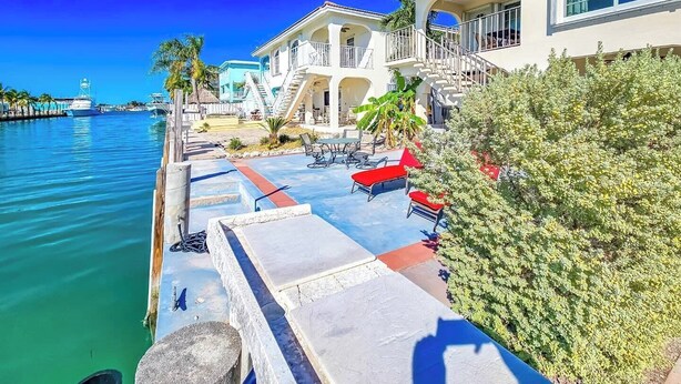 A waterfront property with a pool, outdoor seating, and a staircase leading to a balcony.