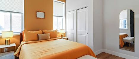 Une chambre avec un grand lit, des tables de chevet, un miroir et une vue sur l’extérieur.