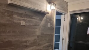 A living room with a brown sofa, a wall-mounted light fixture, and a door leading to a closet. - Private cabin on 5 acres with WiFi, AC & pet friendly  (Curra)