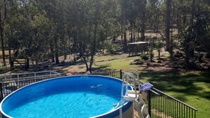 A round above-ground pool with a metal ladder and a safety fence, surrounded by a grassy area and trees. - Private cabin on 5 acres with WiFi, AC & pet friendly  (Curra)