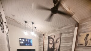 A living room with a black leather sofa, a flat-screen TV, a ceiling fan, and artwork on the walls. - Private cabin on 5 acres with WiFi, AC & pet friendly  (Curra)