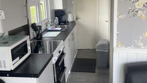 A compact kitchen with white cabinets, a microwave, a coffee maker, and a sink. - Charming Chalet Nestled in Heart of Clarach Bay (Aberystwyth)
