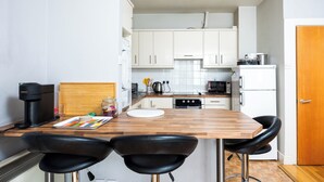 Una cocina compacta con armarios blancos, una encimera de madera, una cafetera y un microondas. Hay dos taburetes negros en la barra de la cocina.