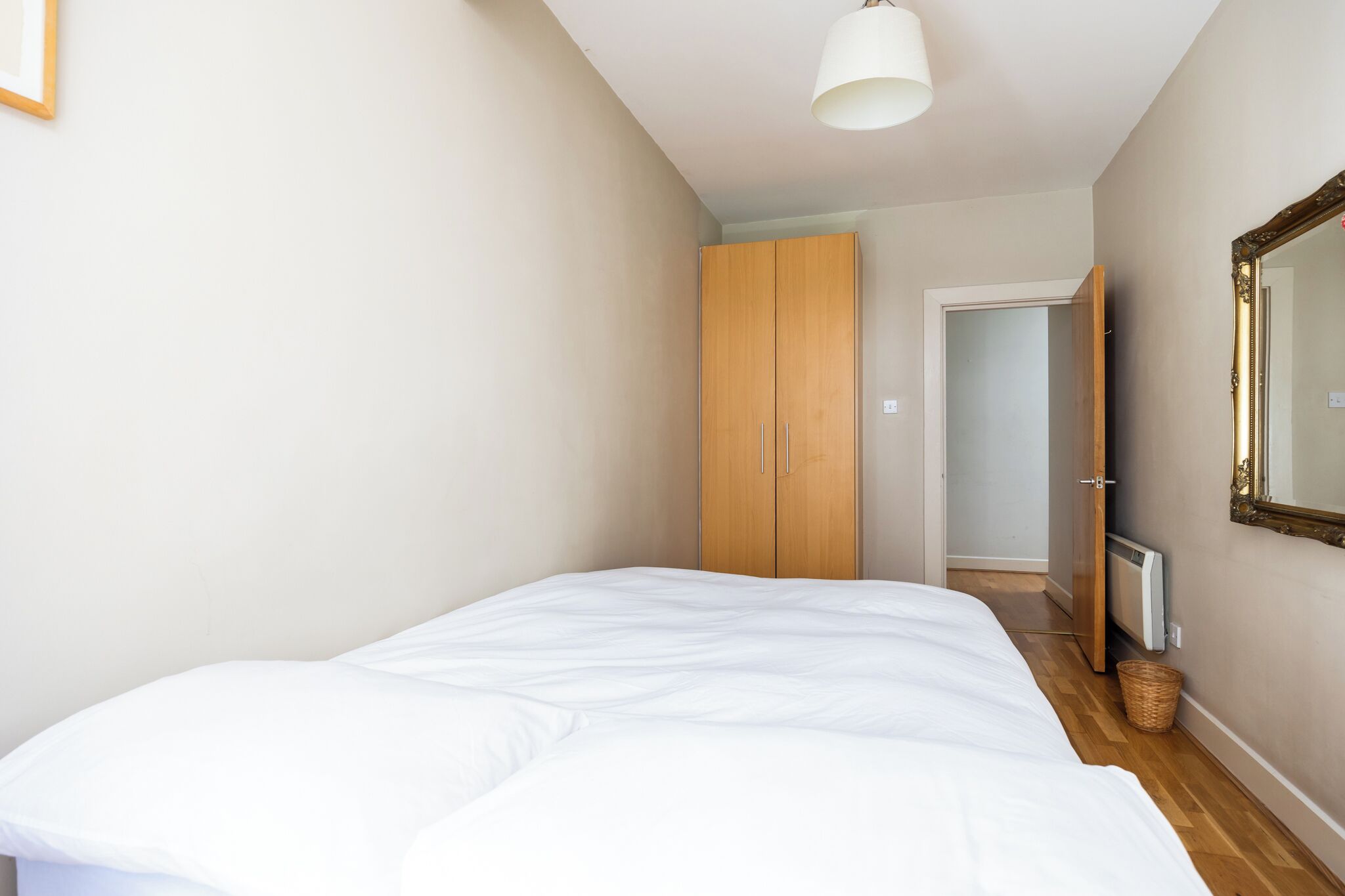 A bedroom with a large bed, wooden wardrobe, and a mirror on the wall.