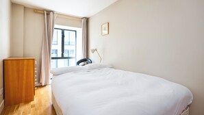 Un dormitorio con cama, cómoda de madera, escritorio con silla y ventana con cortinas.
