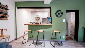 A modern kitchen with a green accent wall, a hanging plant, a clock, and three stools. - Douce vie en Provence  (Malaucène)