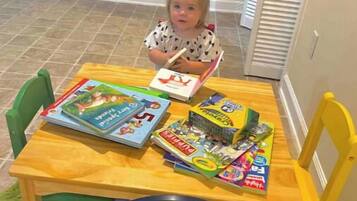 Ein Kind sitzt an einem Holztisch mit verschiedenen Kinderbüchern und Spielsachen.