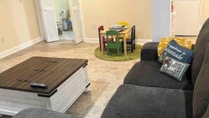 A living room with a gray sofa, a coffee table, and a dining area with a table and chairs. - Country farm cottage (Nesmith)