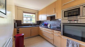 Una cocina moderna con armarios de madera, horno empotrado y ventana con vistas a un balcón.