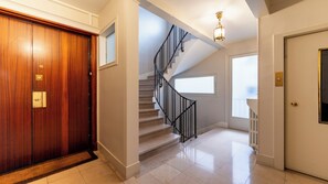 A hallway with a wooden door, a staircase with a black railing, and a radiator. - Spacious 3BD Family Apartment, Auteuil (Paris)