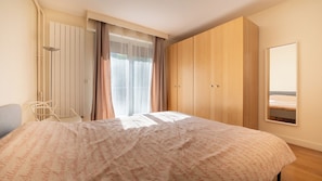 A bedroom with a bed, a chair, a wardrobe, and a window with curtains. - Spacious 3BD Family Apartment, Auteuil (Paris)